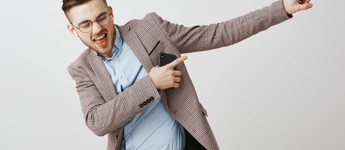 Boosting mood and confidence with right track. Delighted good-looking joyful man with bristle in trendy jacket singing dancing pointing at upper right corner listening music in wireless earbuds Boosting mood and confidence with right track. Delighted good-looking joyful man with bristle in trendy jacket singing dancing pointing at upper right corner listening music in wireless earbuds. Emotions and technology concept